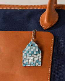 Keychain with a blue geometric design attached to a brown leather bag.