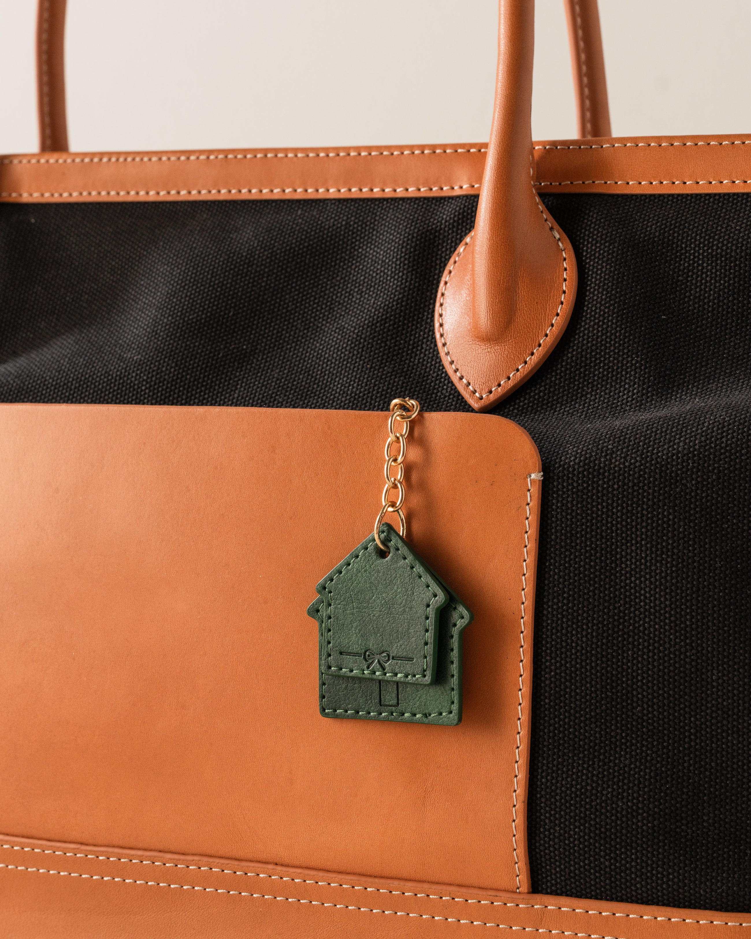 Green house-shaped keychain attached to a brown and black bag.