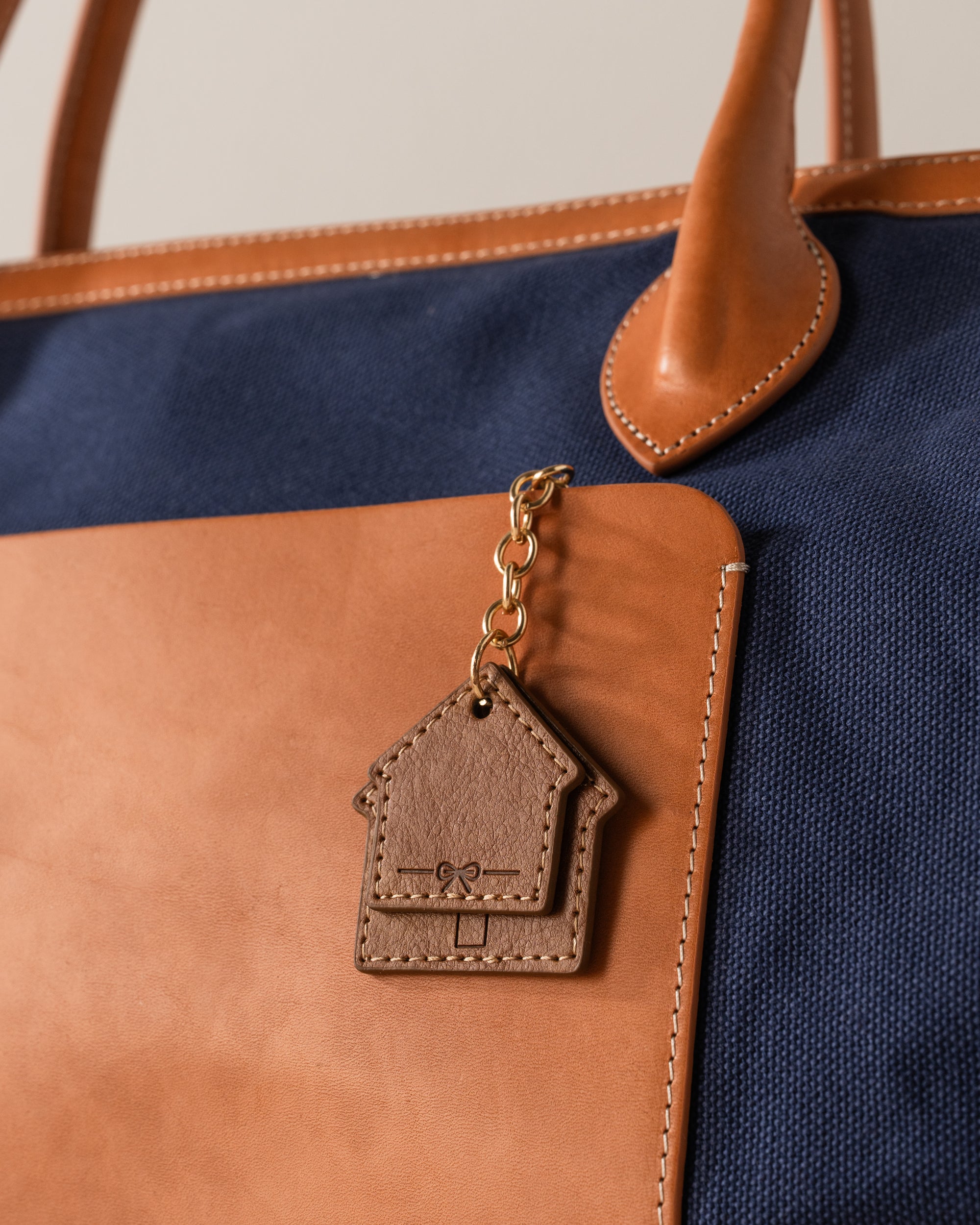 Brown leather keychain attached to a brown and navy bag